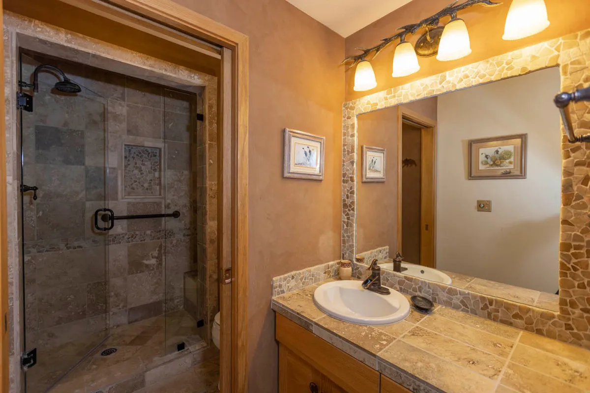 A modern and tranquil bathroom featuring a spacious shower area, vanity with sink, and a large mirror. The clean lines and soft lighting create a relaxing ambiance, perfect for unwinding and personal care after outdoor adventures.