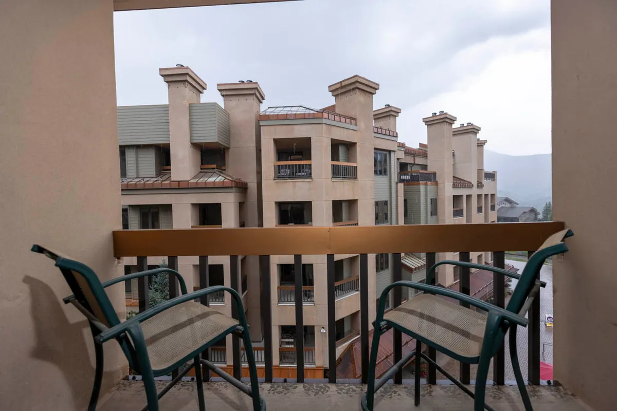 Another inviting exterior balcony scene, featuring a sturdy railing, two chairs, and the distinctive architecture of adjacent buildings. The calm, reflective mood suggests leisure time spent enjoying the fresh air, perhaps sharing a laugh or simply taking in the village's sights and sounds.