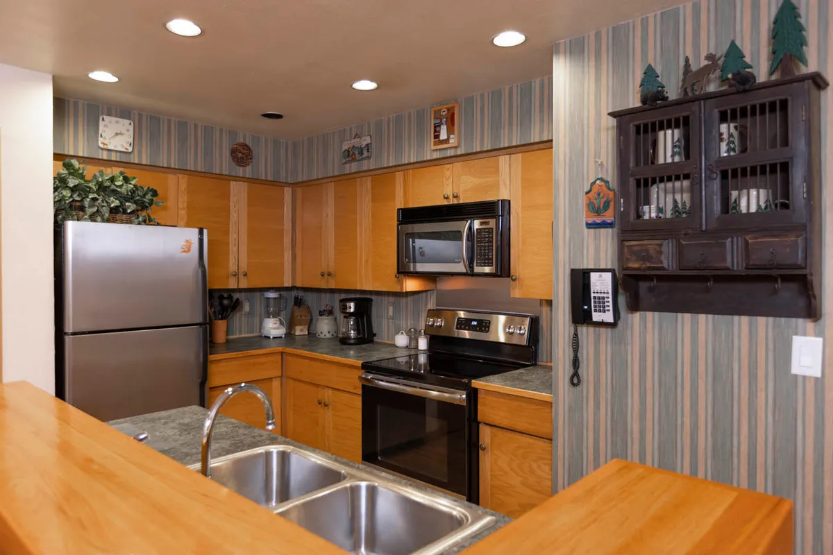 A cozy kitchen nook with a stainless steel refrigerator, black stove and microwave, wooden cabinets, and a decorative shelf adorned with knick-knacks. The atmosphere is welcoming and homey, ideal for cooking and entertaining.