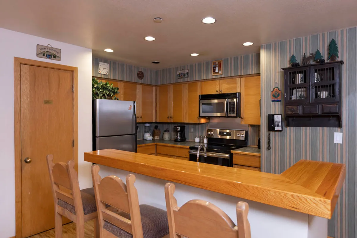 A bright, inviting kitchen featuring a central island, modern stainless steel appliances, ample wooden cabinetry, and a striped wallpaper that adds a touch of charm. The spacious layout is perfect for preparing meals or gathering around the island for conversation.