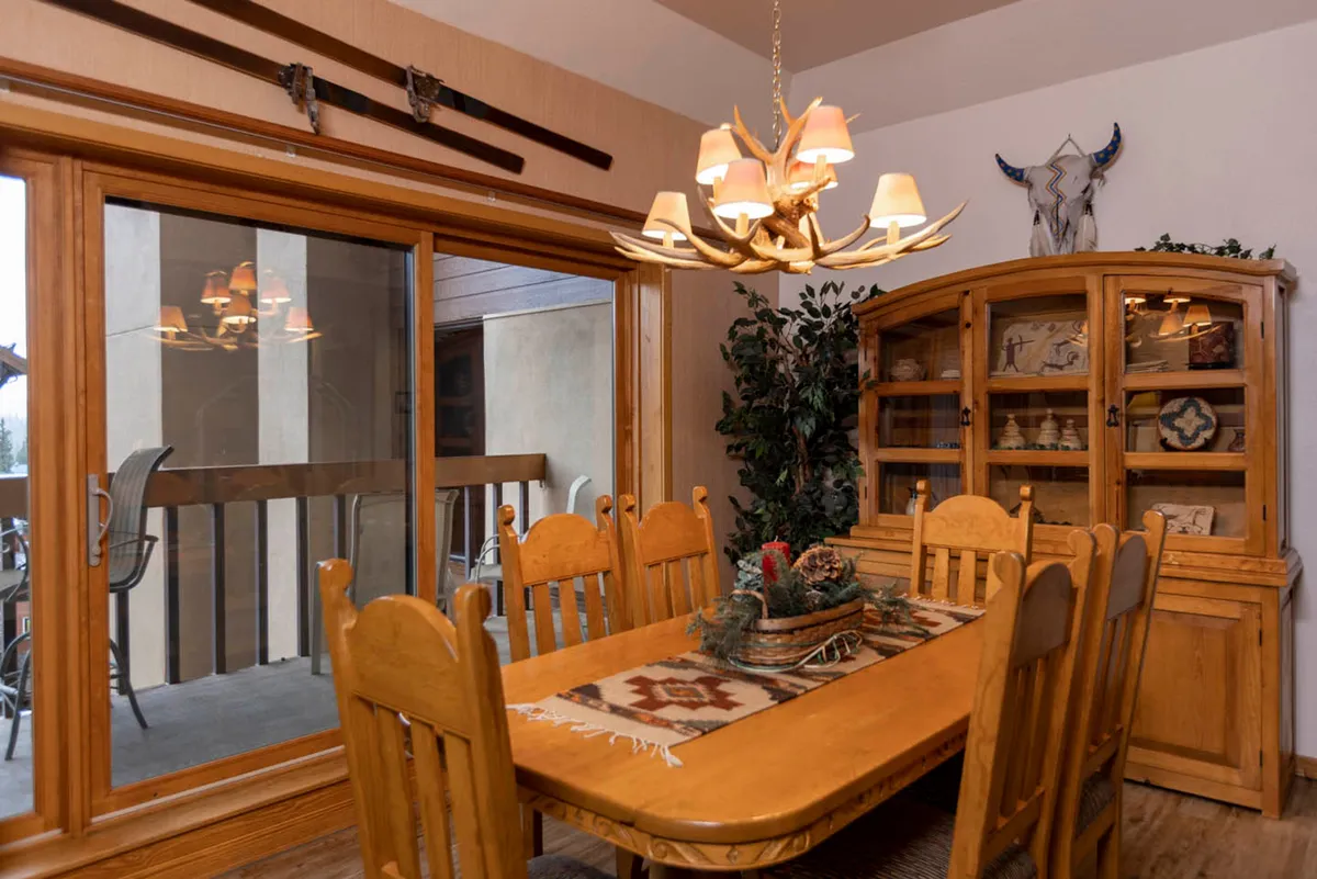 The scene highlights a warm and welcoming dining area with a large wooden table beneath a stylish chandelier. A window offers a glimpse of the outdoors, while decorative accents add to the sense of comfort and hominess.